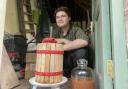 Joshua Dyer crouched behind a cider press and a demijohn
