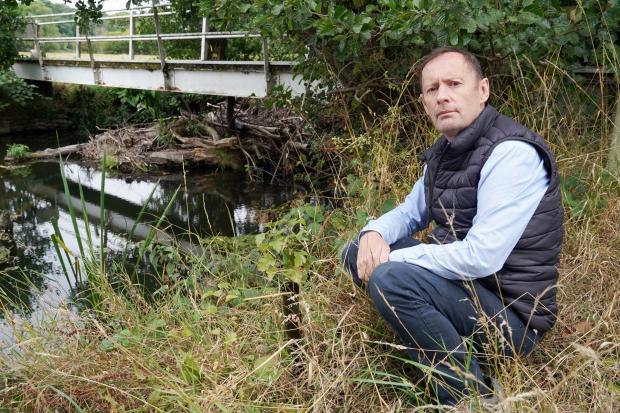 Coun Roger Phillips on the riverbank near the footpath bridge which has been closed due to the build up of wood debris.