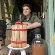 Joshua Dyer crouched behind a cider press and a demijohn